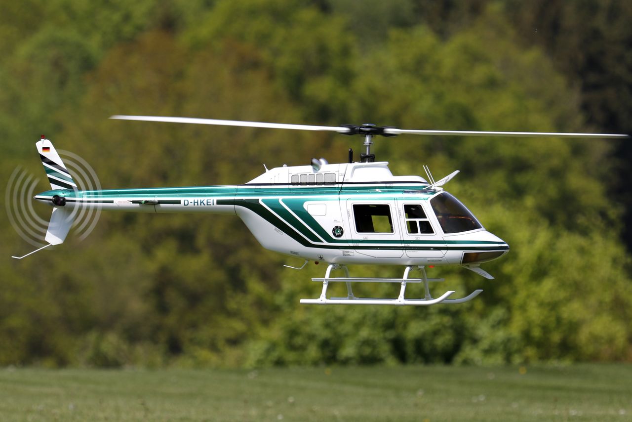 Close-up of a remote controlled white helicopter flying outdoors against a green backdrop.