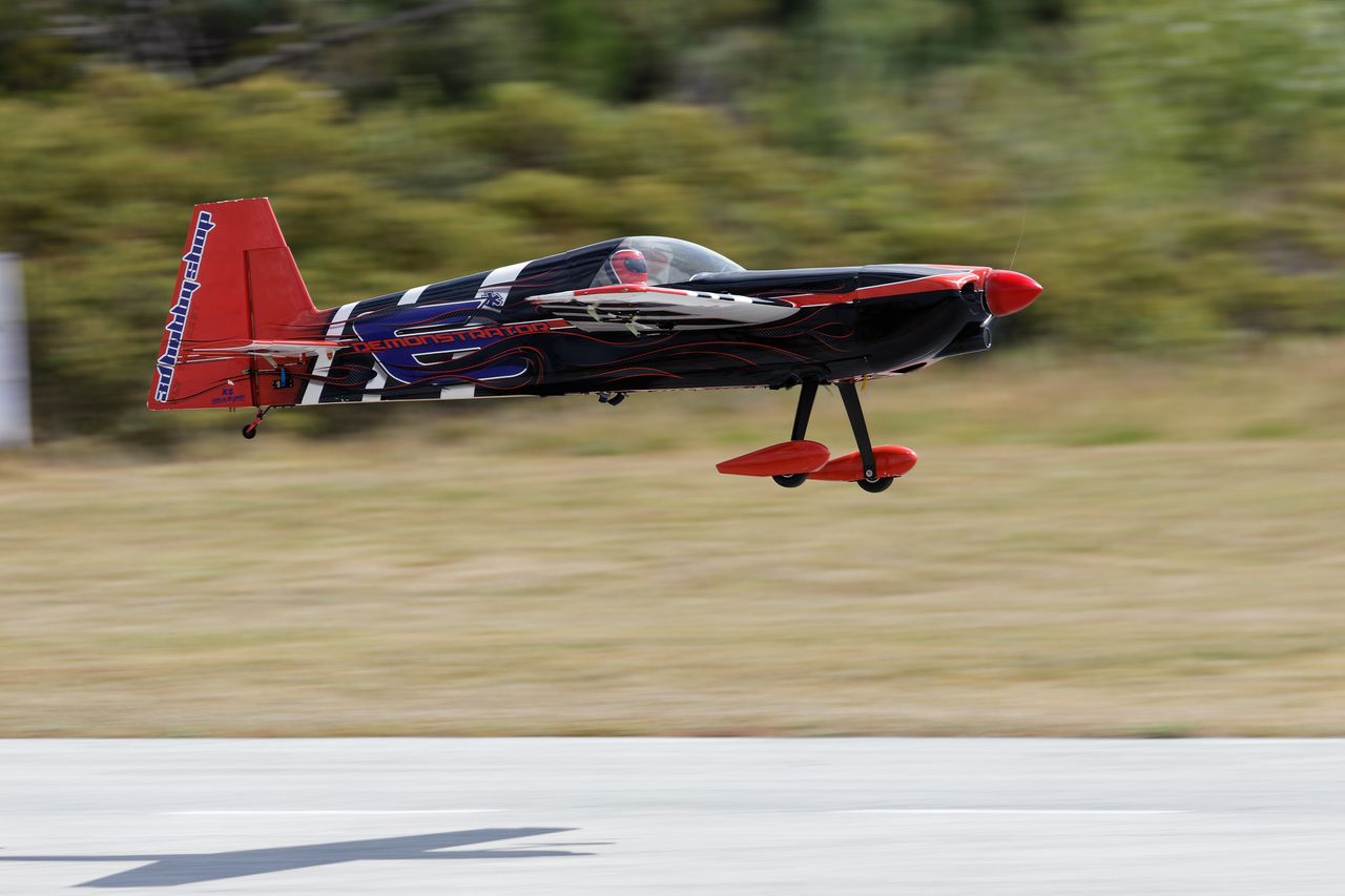 High-speed black and red model aircraft flying low over tarmac outdoors.
