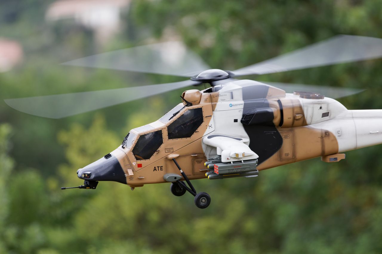 A detailed shot of a radio-controlled helicopter with a camouflage design flying outdoors.