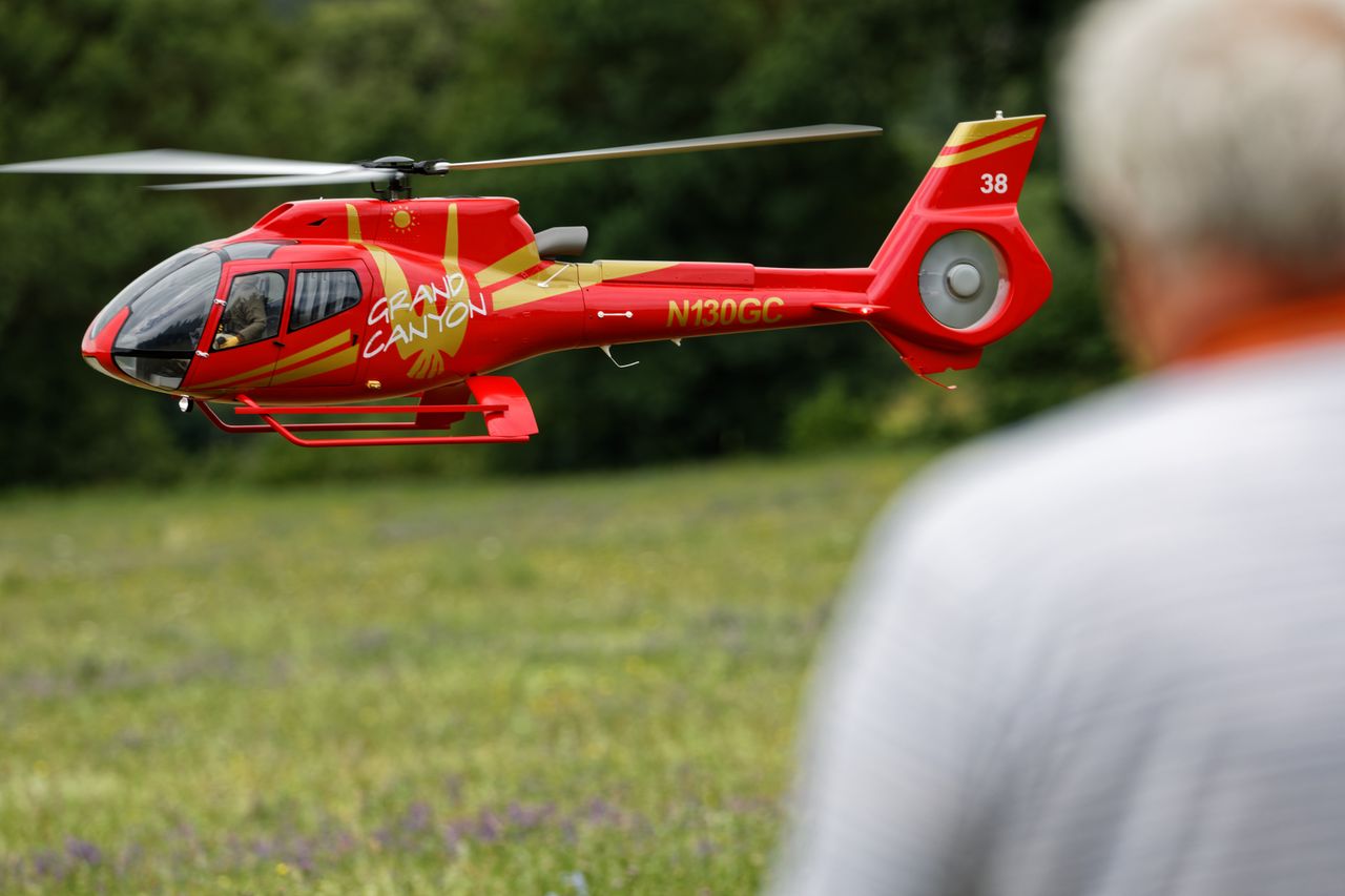 A vibrant red remote control helicopter flies outdoors over a grassy field.